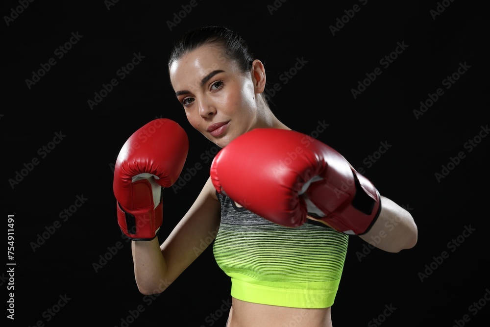 Beautiful woman in boxing gloves training on black background