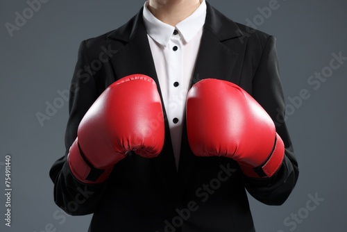 Businesswoman in suit wearing boxing gloves on grey background, closeup © New Africa