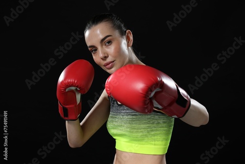 Beautiful woman in boxing gloves training on black background