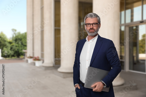 Successful lawyer with laptop near building outdoors, space for text