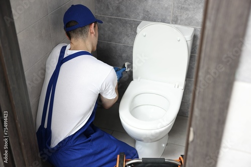 Billede på lærred Plumber with spanner repairing toilet bowl in water closet