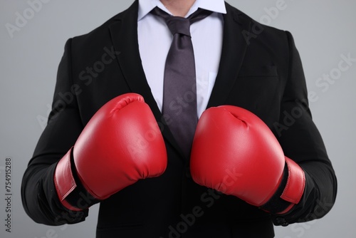 Businessman in suit wearing boxing gloves on grey background, closeup © New Africa
