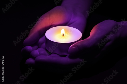 Woman holding burning violet candle in hands on black background, closeup. Funeral attributes