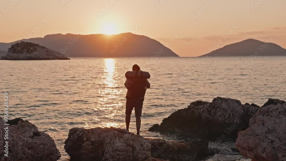 Male tourist with a backpack meets the sunrise by the sea on the island Male tourist with a backpack meets the sunrise by the sea on the island