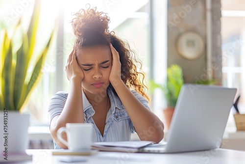 Young beautiful mixed raced womanhad astrong headache. Sitting at a desk with a laptop. photo