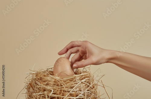 Hand picking egg from straw nest on beige background, Easter concept, minimalistic composition