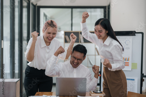 Slika na platnu Three ecstatic asian business professionals celebrating a victory with a fist pump in a modern office
