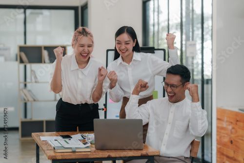 Three ecstatic asian business professionals celebrating a victory with a fist pump in a modern office.