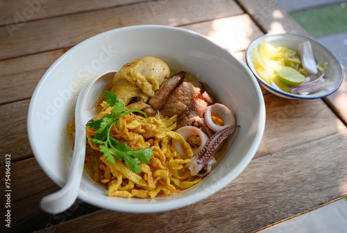 A bowl of Khao Soi, a Northern Thai coconut curry noodle soup with chicken, seafood, and crispy noodles, served with lime and pickled vegetables.
