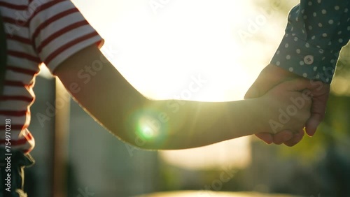 Happy family mother and daughter holding hands walking together at bright sun light summer park closeup. Little baby kid child and female parent arm enjoy outdoor weekend activity with love tenderness photo
