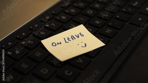 view from side of yellow sticky note with handwritten words "On Leave" and a smiley, placed on keyboard