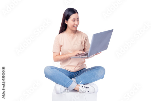 Happy young asian woman sitting on white chair with legs crossed and using laptop computer on light pink background copy space Full body young smiling happy female wearing t shirt and jeans lifestyle	
