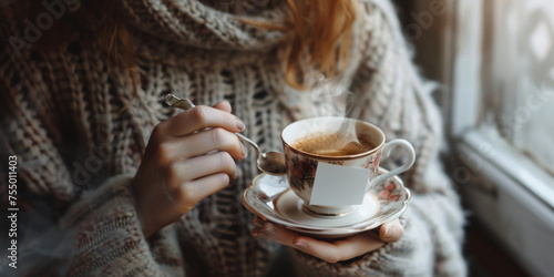 Hands holding a steaming cup of tea with a warm knitted sweater backdrop