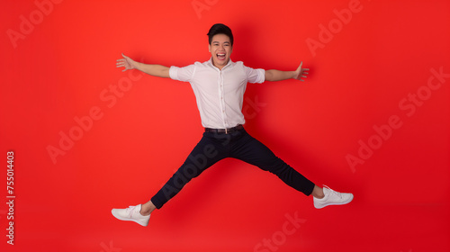 Full body of young dynamic handsome Asian man smiling and jumping with arms outstretched isolated on Coral color background professional photography