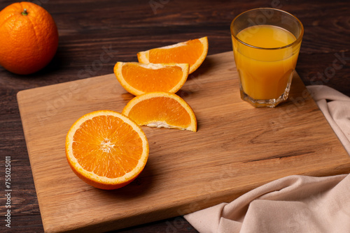 Few slices of orange and a glass of juice on a wooden cutting board.