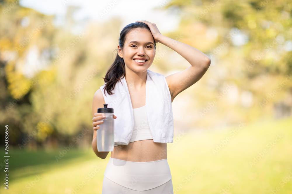 A radiant, smiling woman takes a break from her workout, holding a water bottle A radiant, smiling woman takes a break from her workout, holding a water bottle