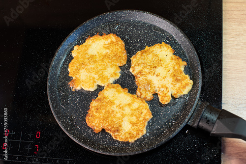 Golden-brown potato pancakes frying in a speckled non-stick pan on a hob. photo