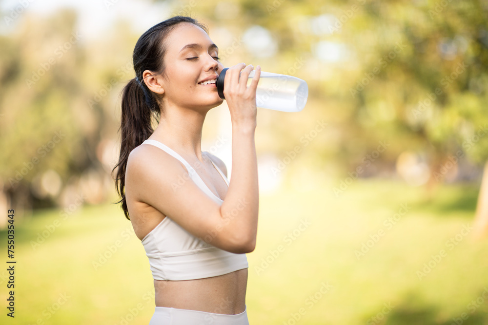 A serene woman in sportswear enjoys a refreshing drink from a water bottle, eyes closed A serene woman in sportswear enjoys a refreshing drink from a water bottle, eyes closed