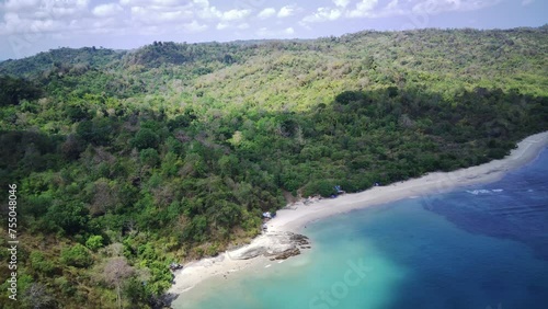 An aerial view of a secluded beach with powdery white sand, turquoise water, and a lush green forest lining the shore. photo