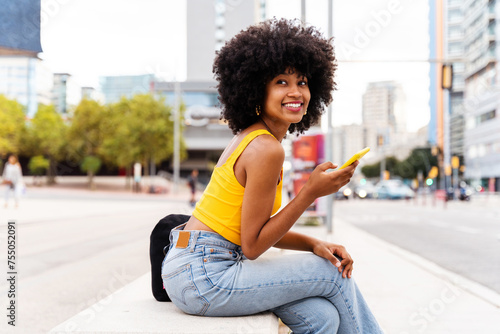 Beautiful young black woman with curly afrp hair style and colorful clothing strolling  outdoors in the city