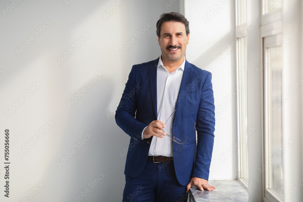 Relaxed and happy middle-aged businessman in a smart blue suit holding eyeglasses Relaxed and happy middle-aged businessman in a smart blue suit holding eyeglasses