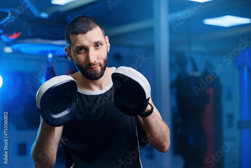 Male boxer instructor holds gloves for practicing punches in boxing ring, blue toning. Concept sport gym training