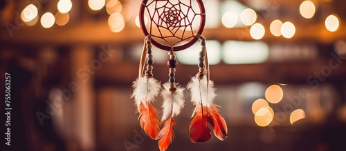 A handmade dream catcher adorned with feathers, threads, and beads is suspended from the ceiling. In the background, soft lights add a warm glow to the scene. photo