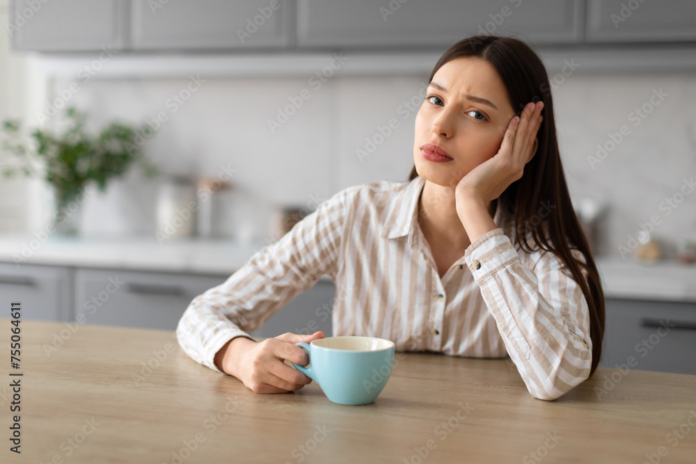 Worried upset woman with coffee cup at kitchen table Worried upset woman with coffee cup at kitchen table