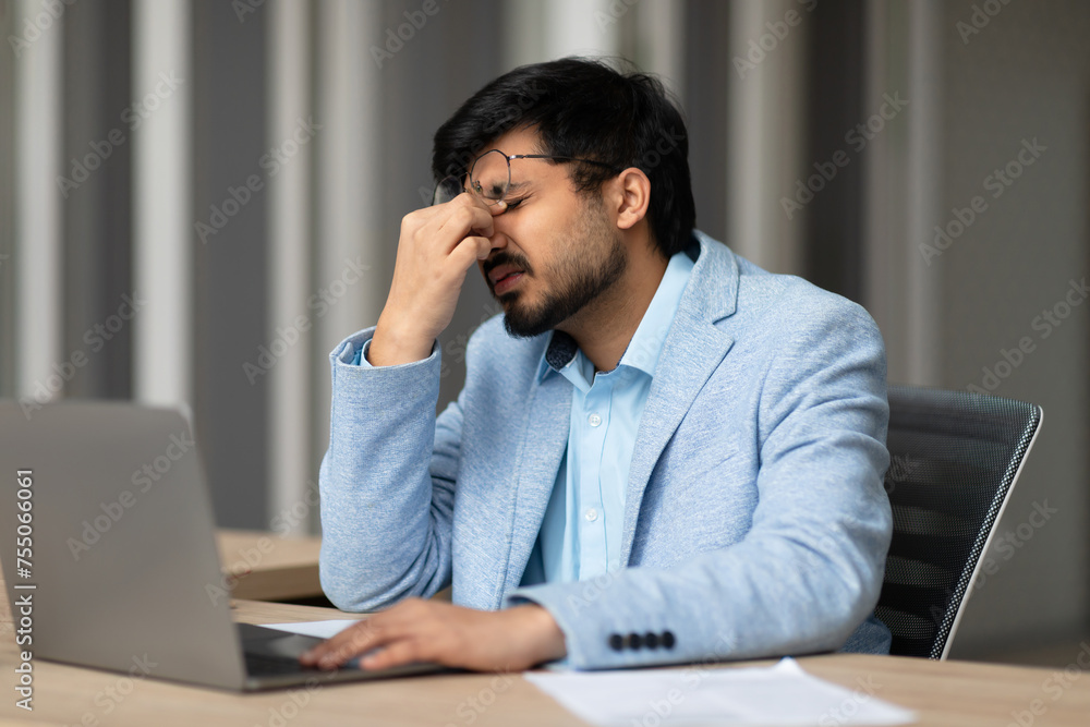 Indian businessman experiencing eye strain sitting tired in office