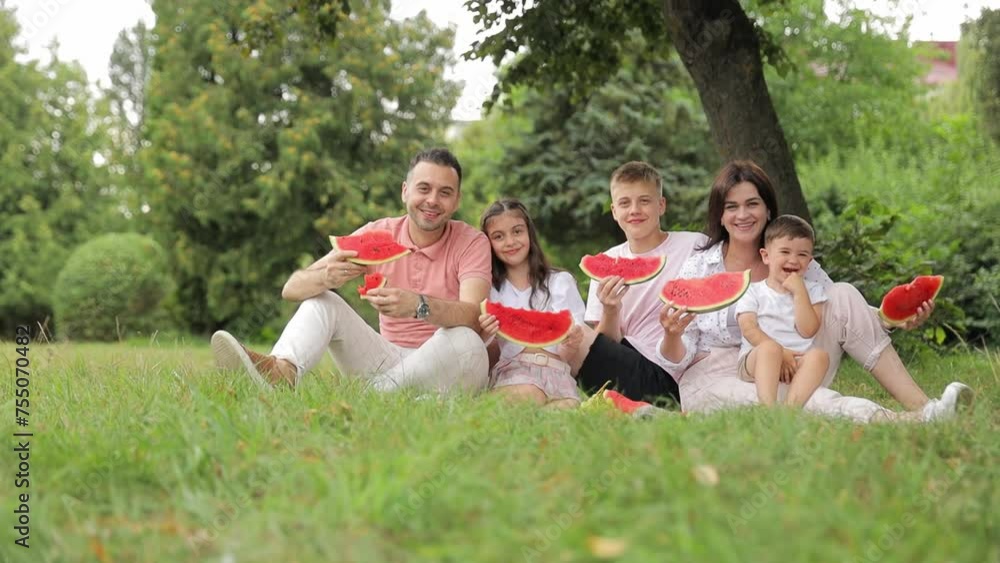 Happy family enjoying watermelon and smiling amidst nature landscape. People in nature, leisure, recreation Happy family enjoying watermelon and smiling amidst nature landscape. People in nature, leisure, recreation