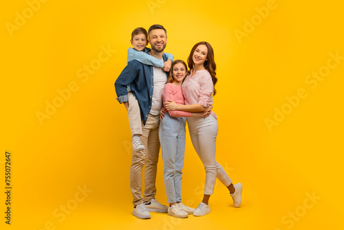 Family Portrait. Happy Young Parents And Their Kids Embracing Over Yellow Background © Prostock-studio