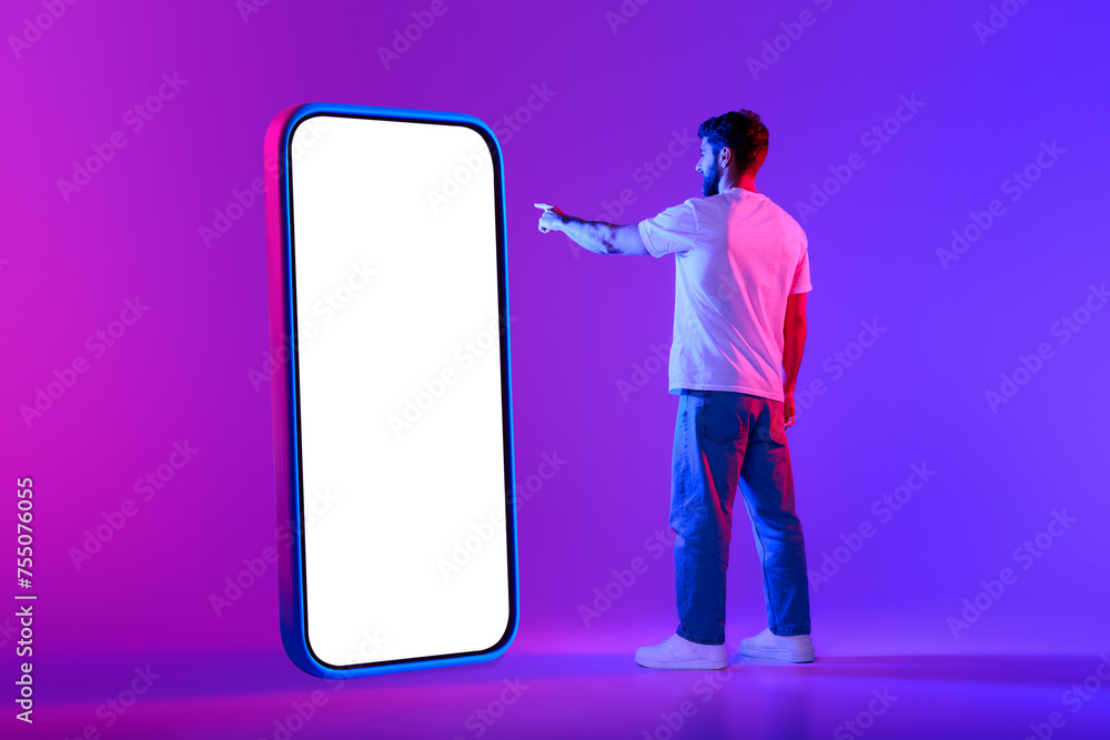 Obraz na plátně Young man points to big cellphone screen against neon backdrop