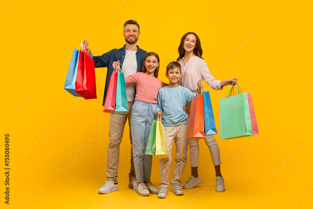Family Shopping. Joyful Young Parents And Their Kids Holding Bright Shopper Bags Family Shopping. Joyful Young Parents And Their Kids Holding Bright Shopper Bags