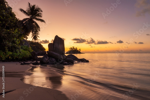 Orange hues of a beautiful sunrise on a romantic beach with palm trees and granite rocks on a tropical island in Seychelles, Africa photo