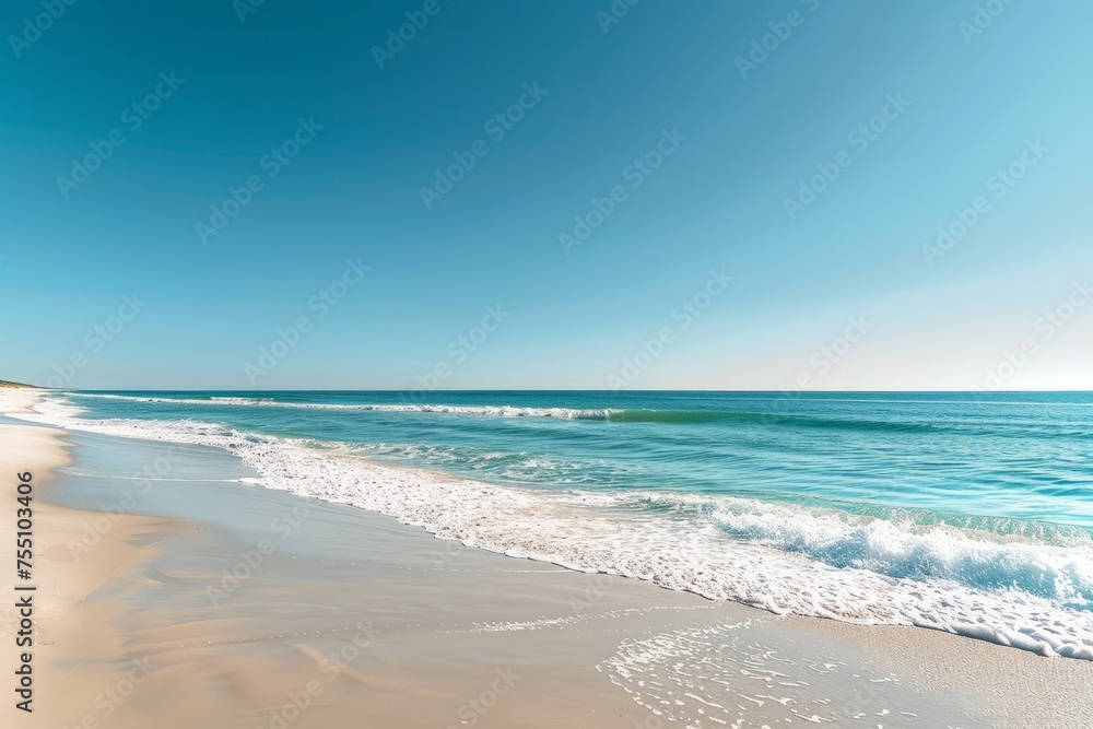 A sandy beach with waves rolling in from the clear blue ocean under a sunny sky.