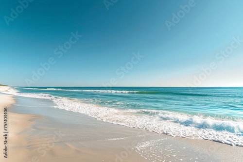 A sandy beach with waves rolling in from the clear blue ocean under a sunny sky.