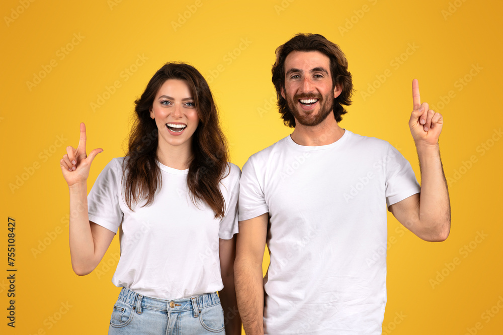 A joyful woman and a man with beards point upwards with bright smiles, wearing white t-shirts A joyful woman and a man with beards point upwards with bright smiles, wearing white t-shirts