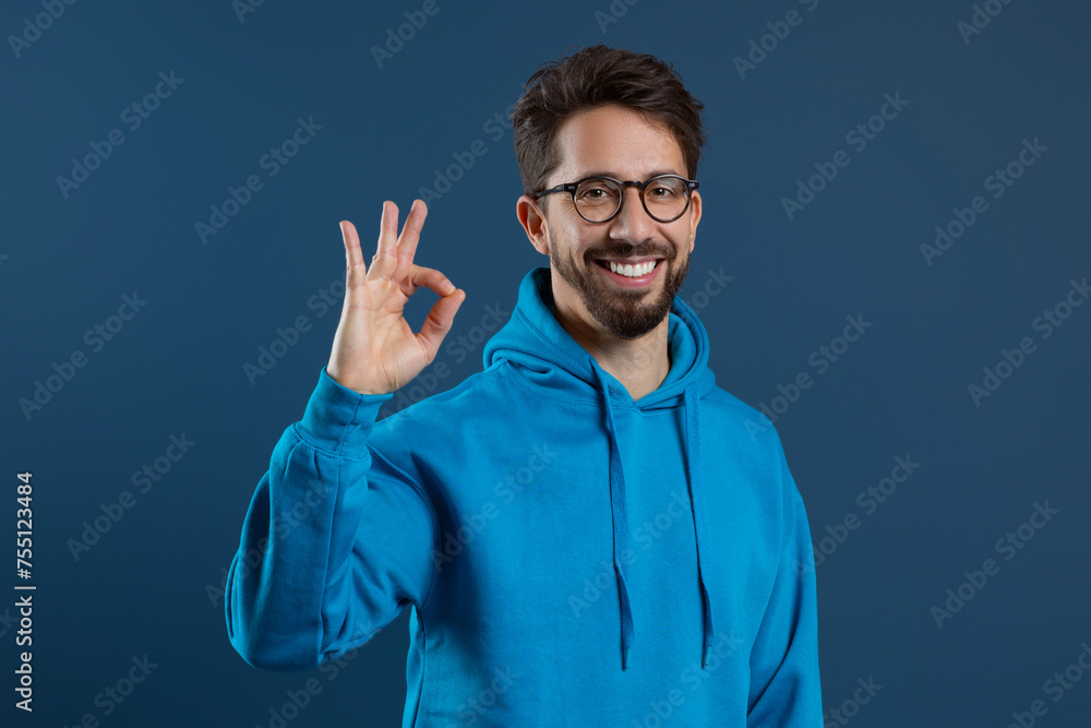 Naklejka premium Happy Young Man Wearing Blue Hoodie Showing Ok Gesture At Camera