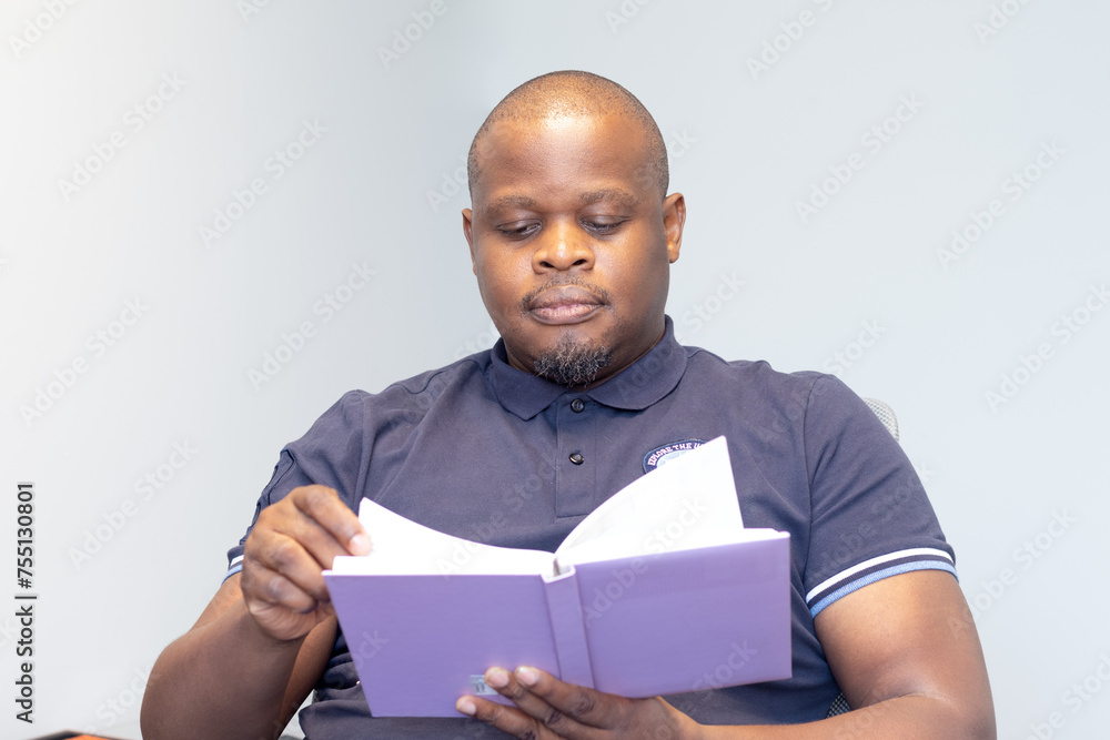 African man seated reading a book with a purple cover African man seated reading a book with a purple cover