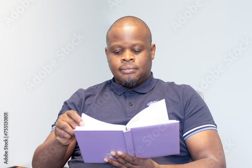 African man seated reading a book with a purple cover