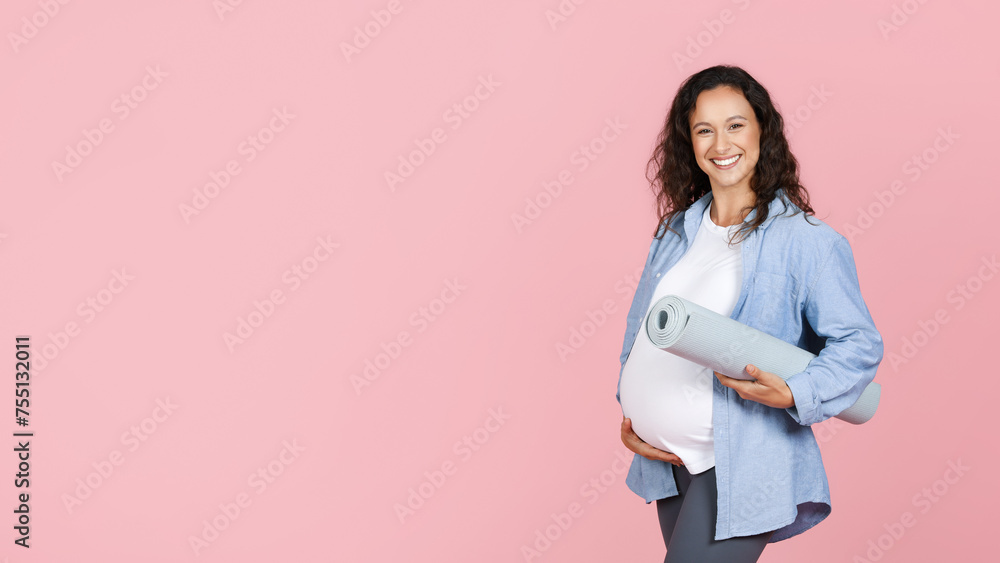 Positive pregnant woman holding fitness mat, pink background Positive pregnant woman holding fitness mat, pink background