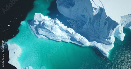 Melting snow covered glacier in blue water aerial top view. Nature beauty towering floating iceberg. Polar winter landscape. Ecology, melting ice, climate change, global warming background. Drone shot photo