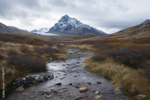 A landscape that includes a clear, flowing stream in the foreground with rocks and sparse vegetation. There is a dominant, sharply pointed mountain peak in the midground, which is rugged.