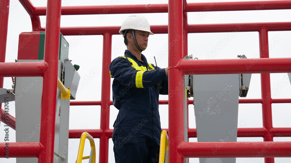 Seaman crew member of cargo vessel equipped with personal protective equipment operate mooring winch from shelter position on cargo ship Seaman crew member of cargo vessel equipped with personal protective equipment operate mooring winch from shelter position on cargo ship