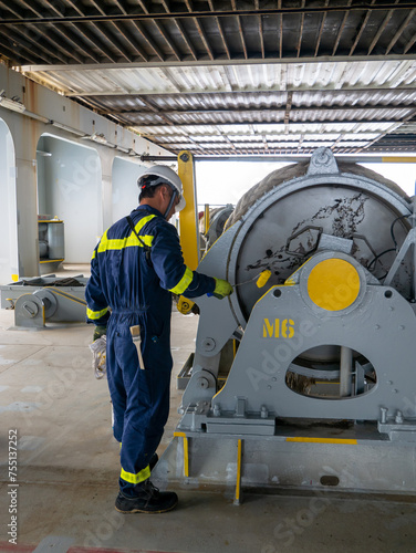 Seaman crew member of cargo vessel  equipped with personal protective equipment is doing maintenance painting of mooring winch on aft station
