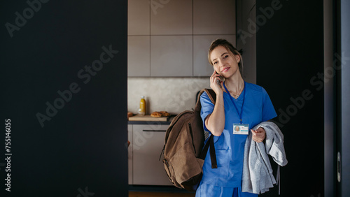 Female doctor getting ready for work, phone calling on smartphone, leaving house in scrubs with backpack. Work-life balance for healthcare worker.