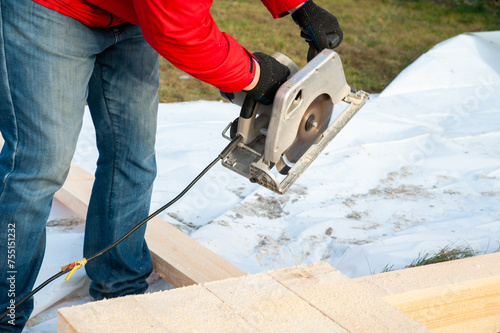 A man in a red jacket cuts boards with a circular saw