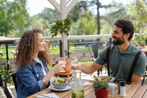 Young couple at date in restaurant, sitting on restaurant terrace. Boyfriend and girlfriend enjoying springtime, having lunch outdoors.