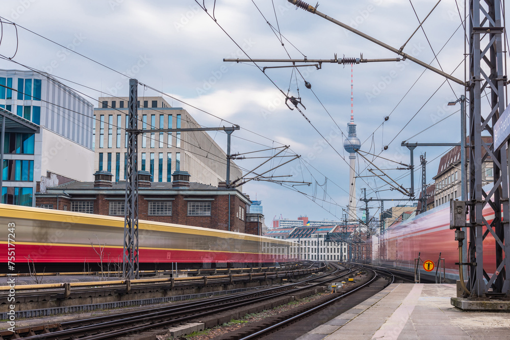 Trains in blur are leaving and approaching the station of Berlin Friedrichstrasse on a cool spring day. Typical houses and TV tower visible in the backgroubd. Train transport in germany, punctuality