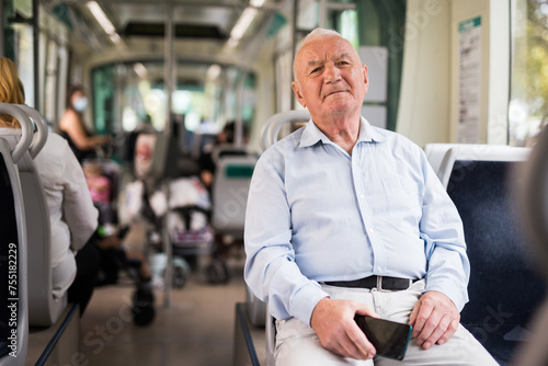 Senior European man sitting on seat inside tram and waiting for his stop.